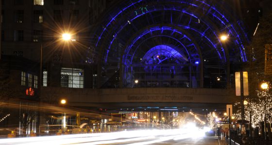 The Artsgarden, a glass building suspended above a street, lit up from the inside at night