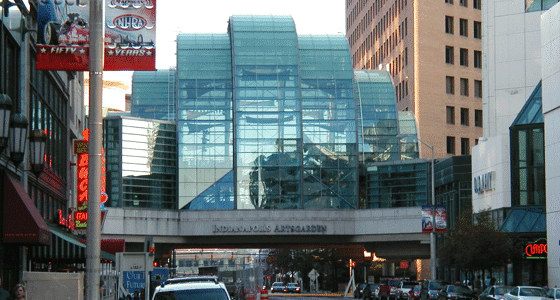 The Artsgarden, a glass building suspended above a street, during the day.
