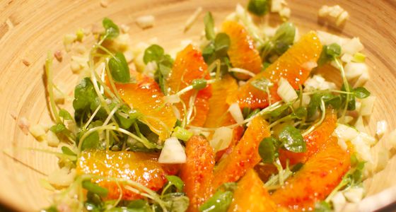 A salad with orange slices, crumbled cheese, and herbs.