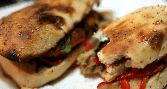 A close-up of a toasted sub sandwich grilled meat, lettuce, and red peppers cut in half.