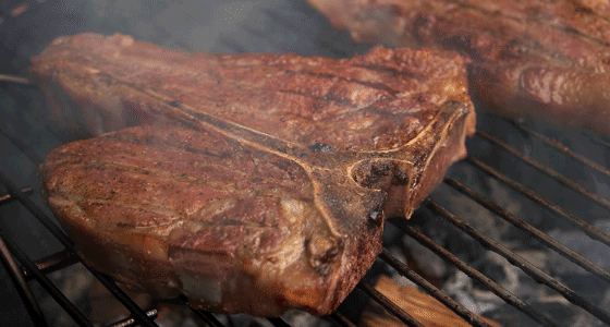 A cooked T-bone steak on a smokey grill.