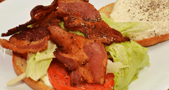 An open face peppered bacon, lettuce, and tomato sandwich with a mayo spread.