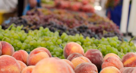 A row of peaches, grapes, and other fruits that go into the distance at an outdoor market.