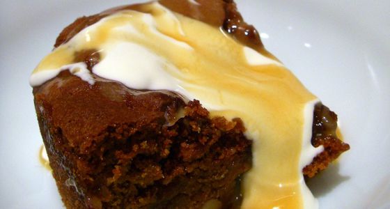 A close-up of sticky toffee pudding with cream on top.