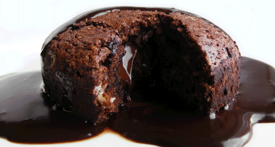 A round chocolate cake split open with chocolate sauce poured over the top.