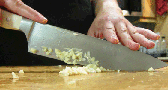 A close up of someone chopping raw onion on a cutting board with a metal kitchen knife.