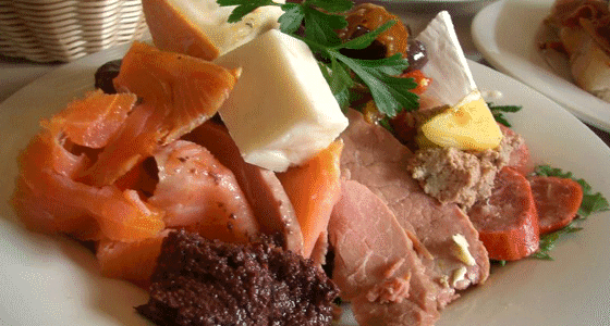 A plate of cold cut slices of various meat, meat spreads, and cheese with lettuce garnish.